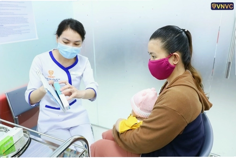 Nhân viên y tế đang hướng dẫn phụ huynh kiểm tra vắc xin trước khi tiêm